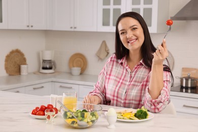 Beautiful overweight woman having healthy meal at table in kitchen