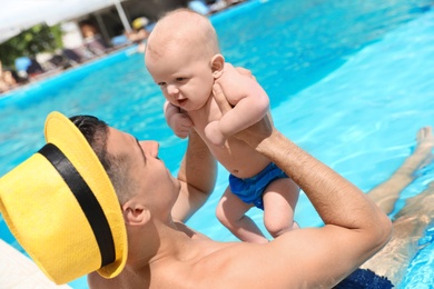 Photo of Man with his little baby in swimming pool on sunny day, outdoors