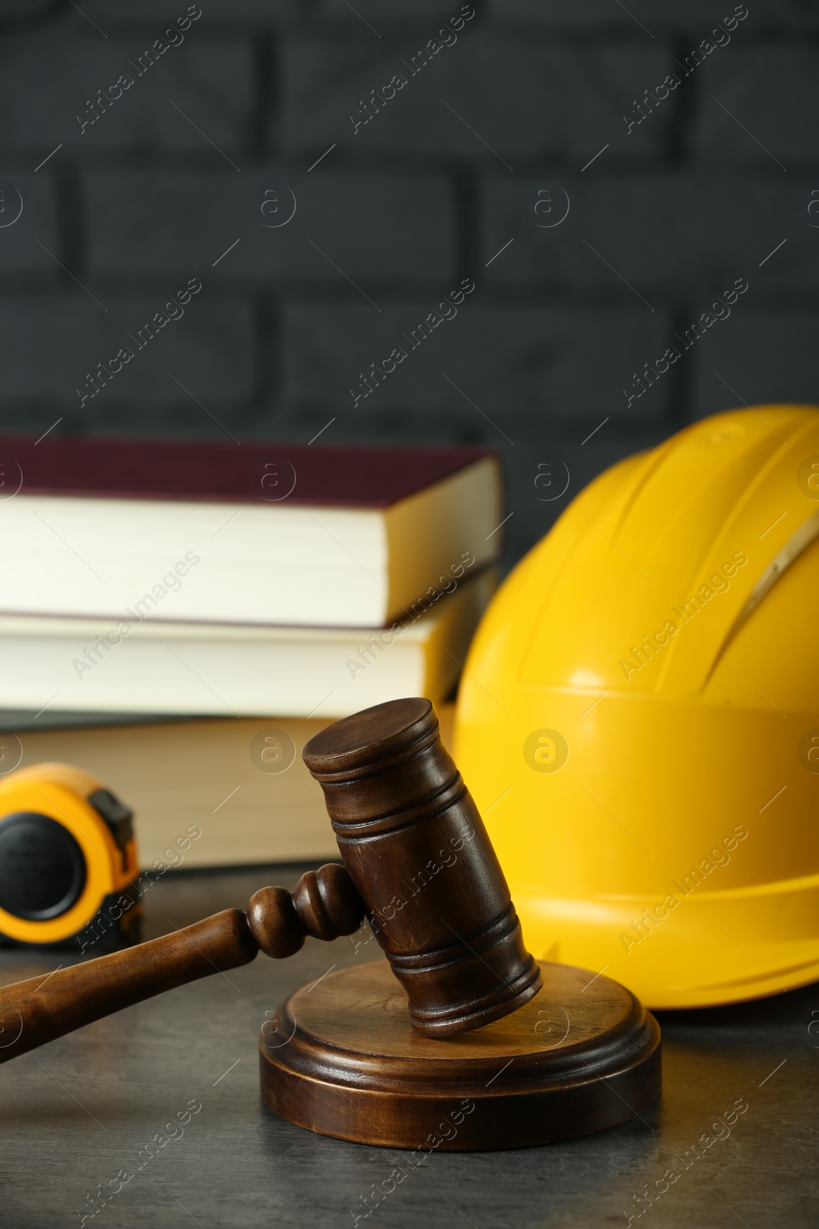 Photo of Construction and land law concepts. Judge gavel, construction helmet, tape measure and books on grey wooden table