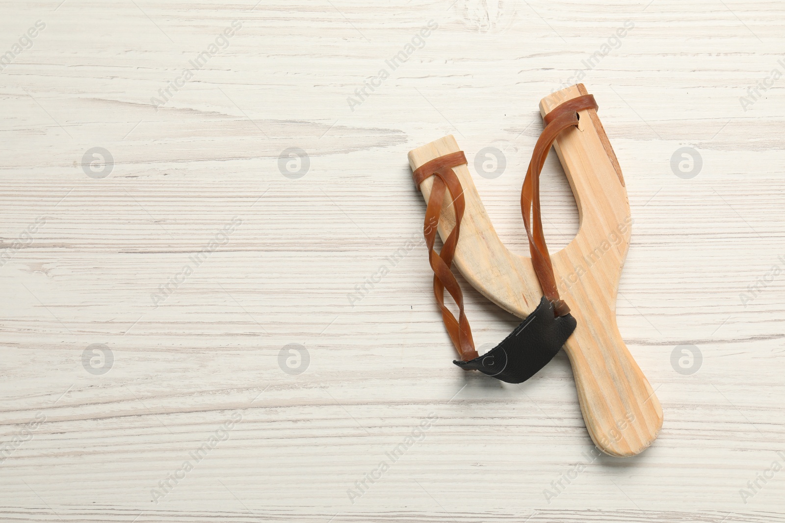 Photo of Slingshot with leather pouch on white wooden background, top view. Space for text