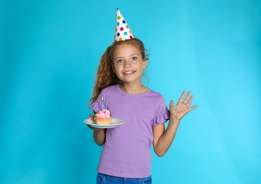 Happy girl holding birthday cupcake with candle on blue background