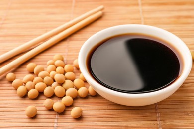 Soy sauce in bowl and soybeans on bamboo mat, closeup