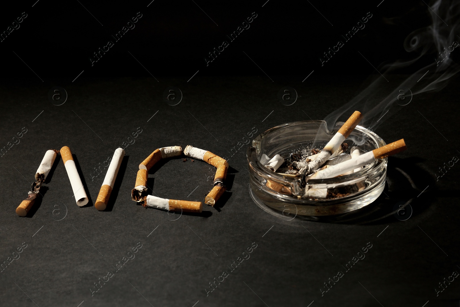 Photo of Word No made with burnt cigarettes and ashtray on black table. Stop smoking concept