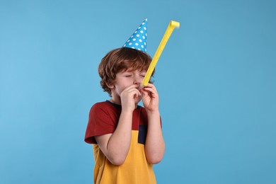 Photo of Birthday celebration. Cute little boy in party hat with blower on light blue background