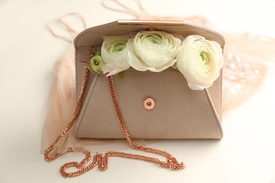 Stylish clutch bag and spring flowers on light background