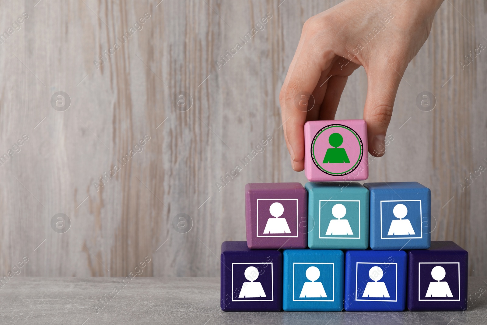 Image of Woman putting cube with green human icon on top of others with white ones on wooden table, closeup