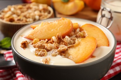 Photo of Tasty peach yogurt with granola and pieces of fruits in bowl on table, closeup