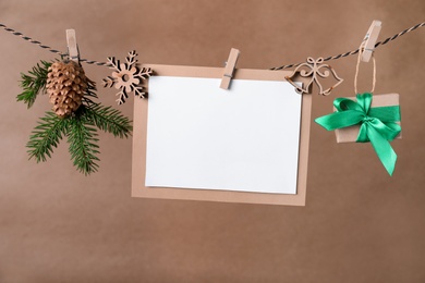 Photo of Blank Christmas card and festive decor on rope against brown background, space for text