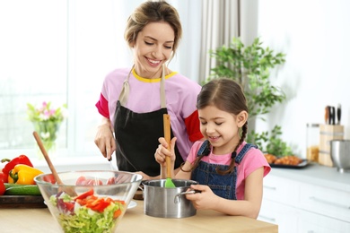 Photo of Young nanny with cute little girl cooking together in kitchen