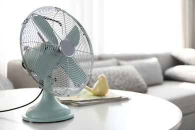 Photo of Modern electric fan on table in living room, space for text. Summer heat