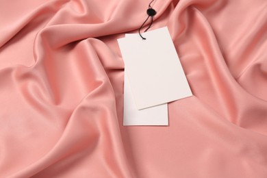 Photo of Blank white tags on pink silky fabric, above view. Space for text