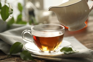 Photo of Pouring milk into cup with tea on wooden table, closeup