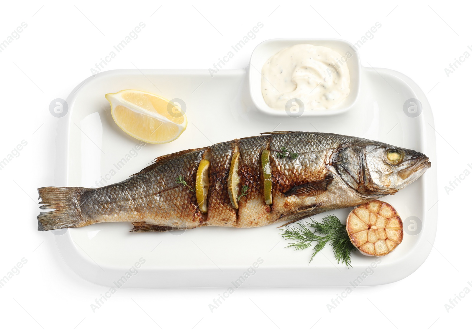 Photo of Plate with delicious roasted sea bass fish, garlic, slice of lemon and sauce on white background, top view