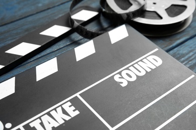 Photo of Clapperboard and reel on wooden table, closeup. Cinema production