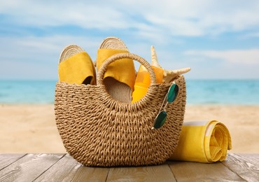 Image of Stylish bag with beach accessories on wooden surface near seashore 