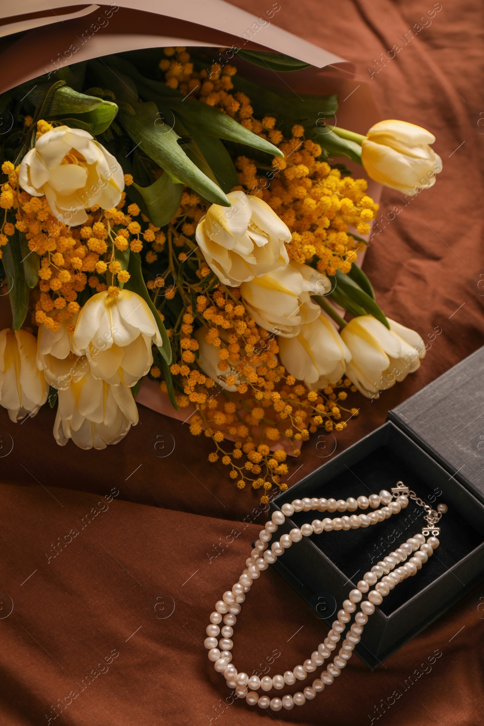 Photo of Bouquet of beautiful spring flowers and necklace on brown fabric, above view