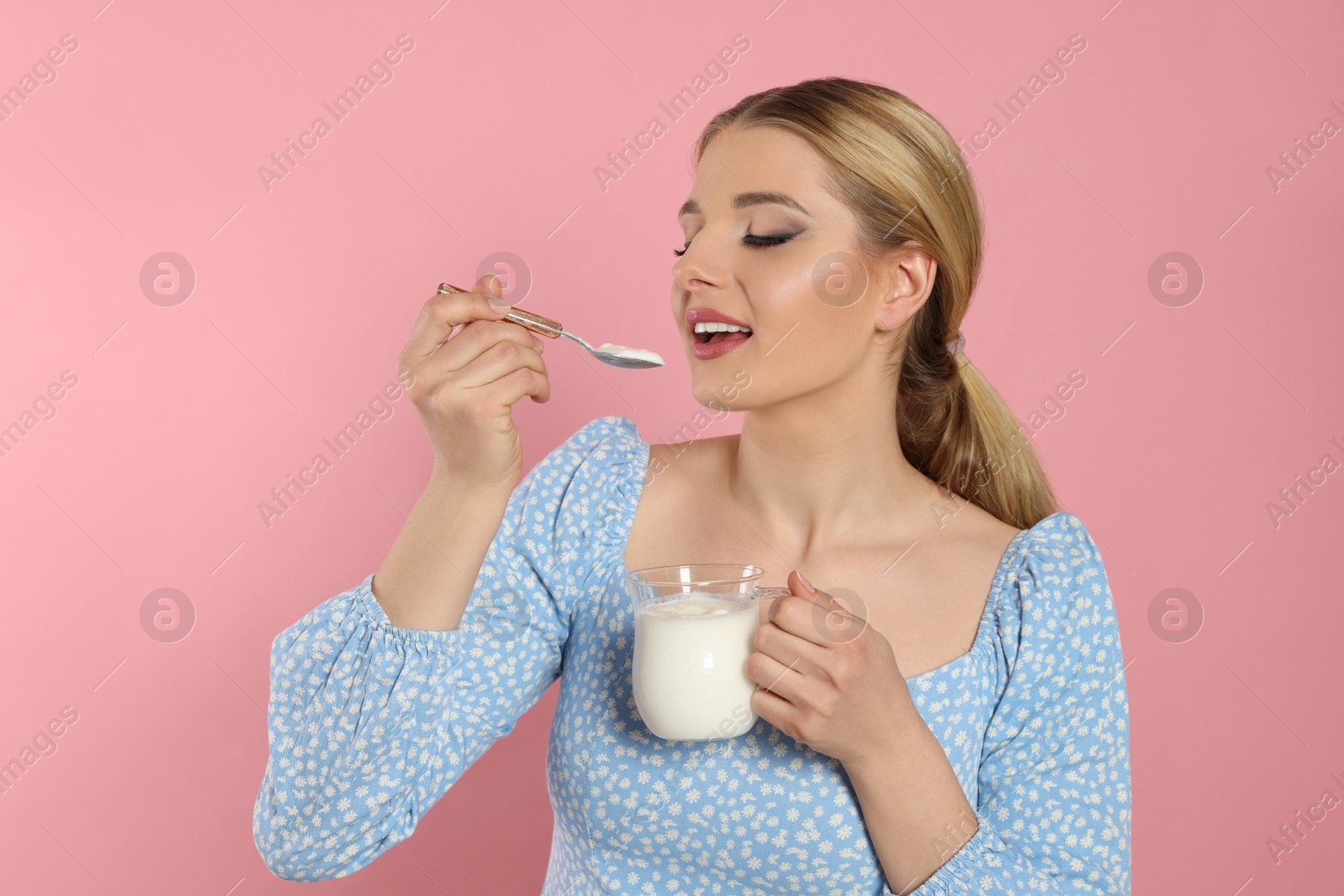 Photo of Happy woman eating tasty yogurt on pink background