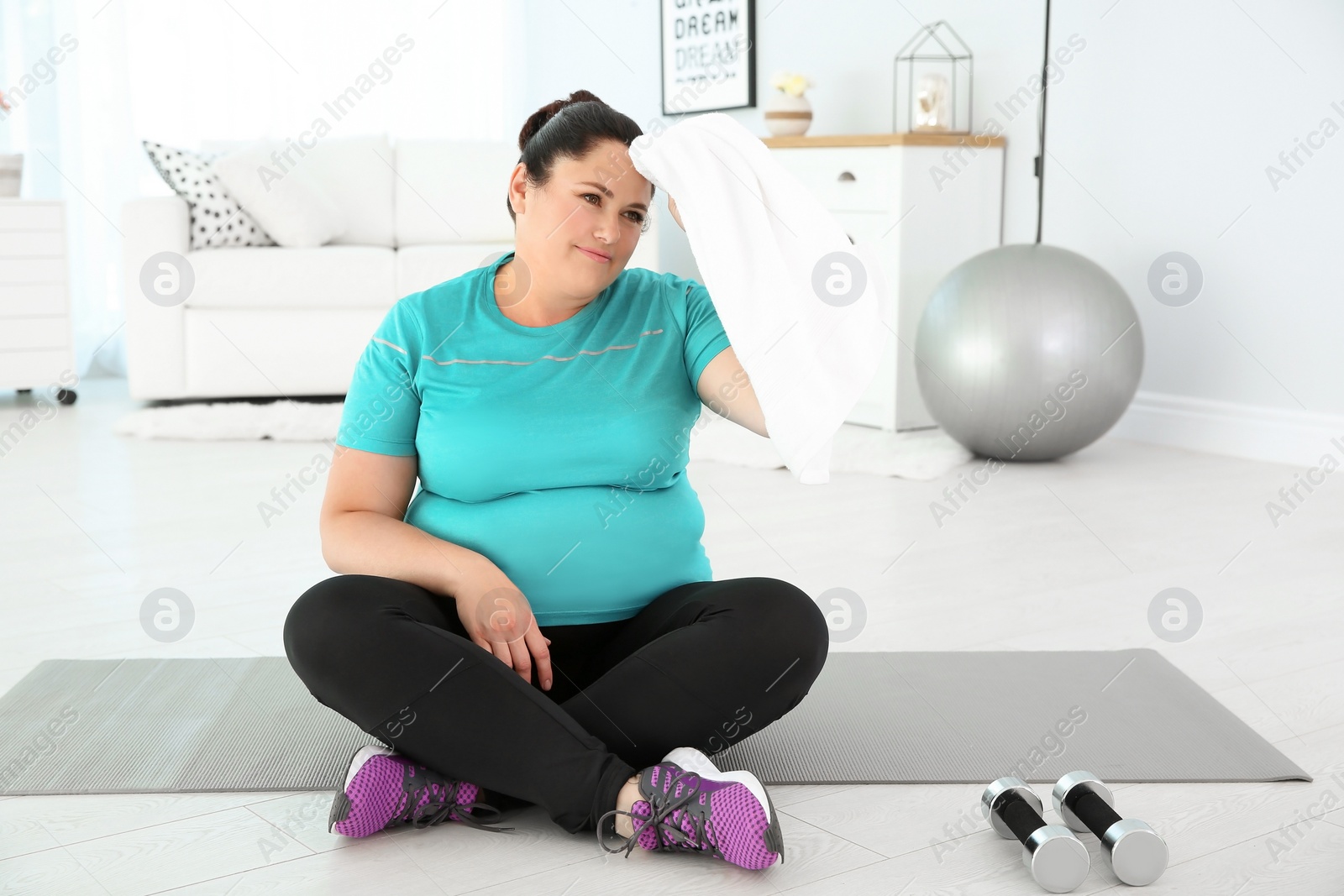 Photo of Tired overweight woman wiping sweat with towel at home