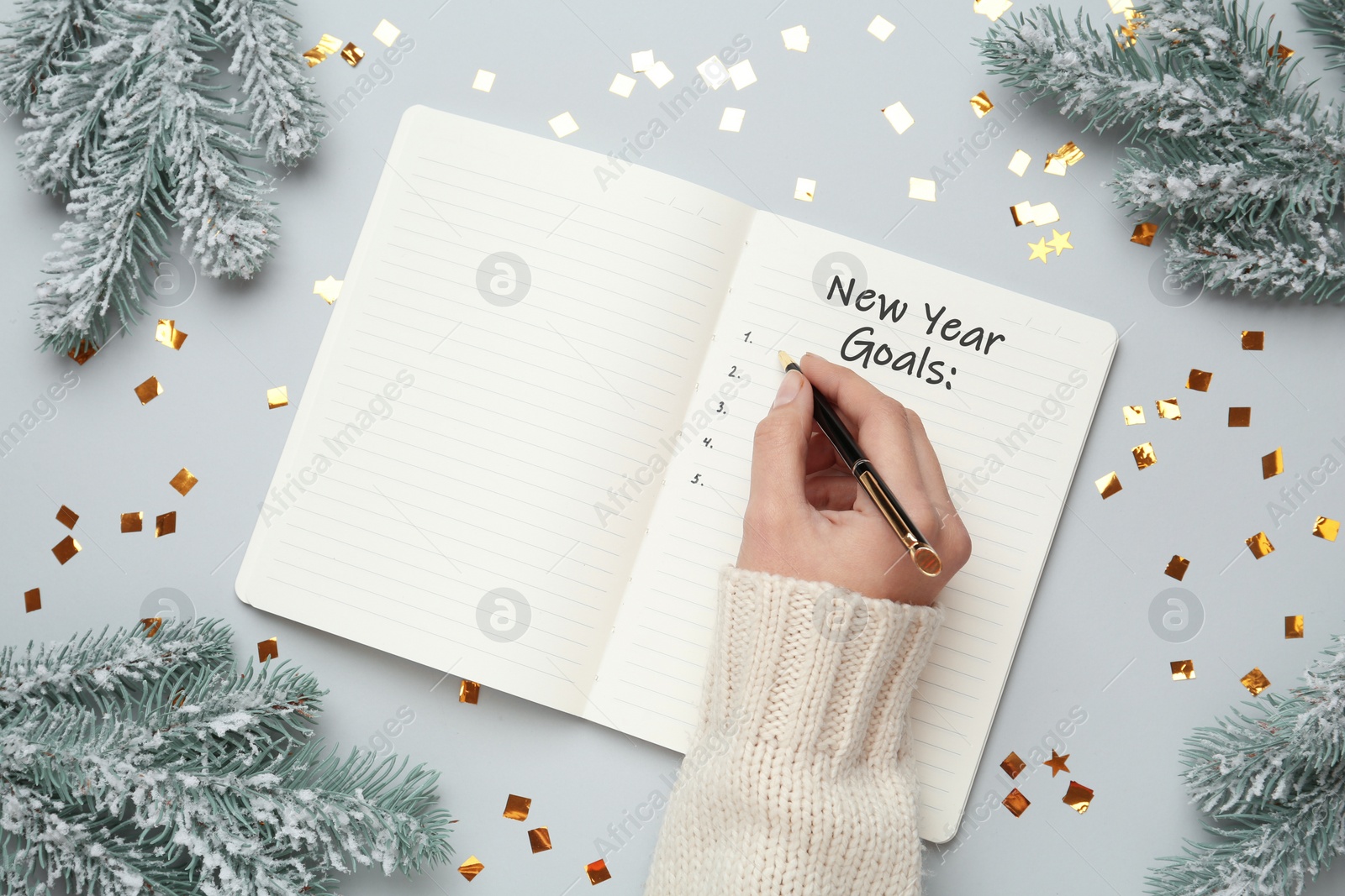 Image of Woman writing in notebook at light grey table with Christmas decor, top view. New Year aims