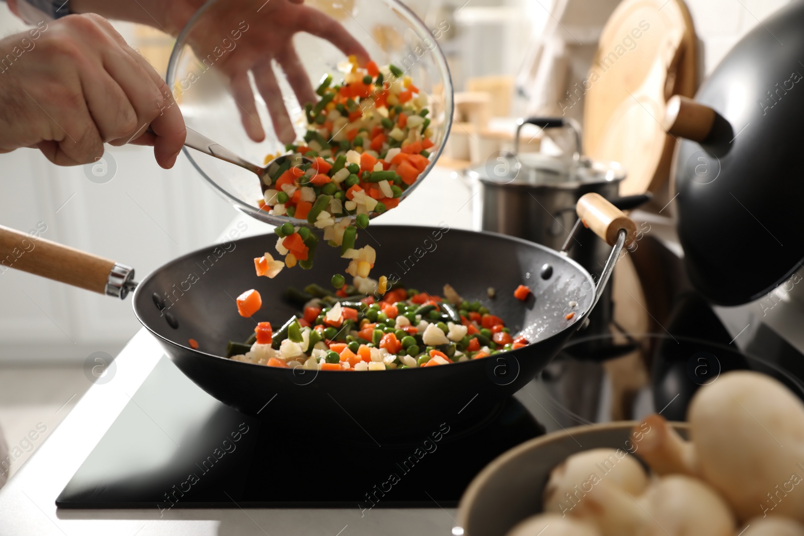 Photo of Man pouring mix of fresh vegetables into frying pan, closeup