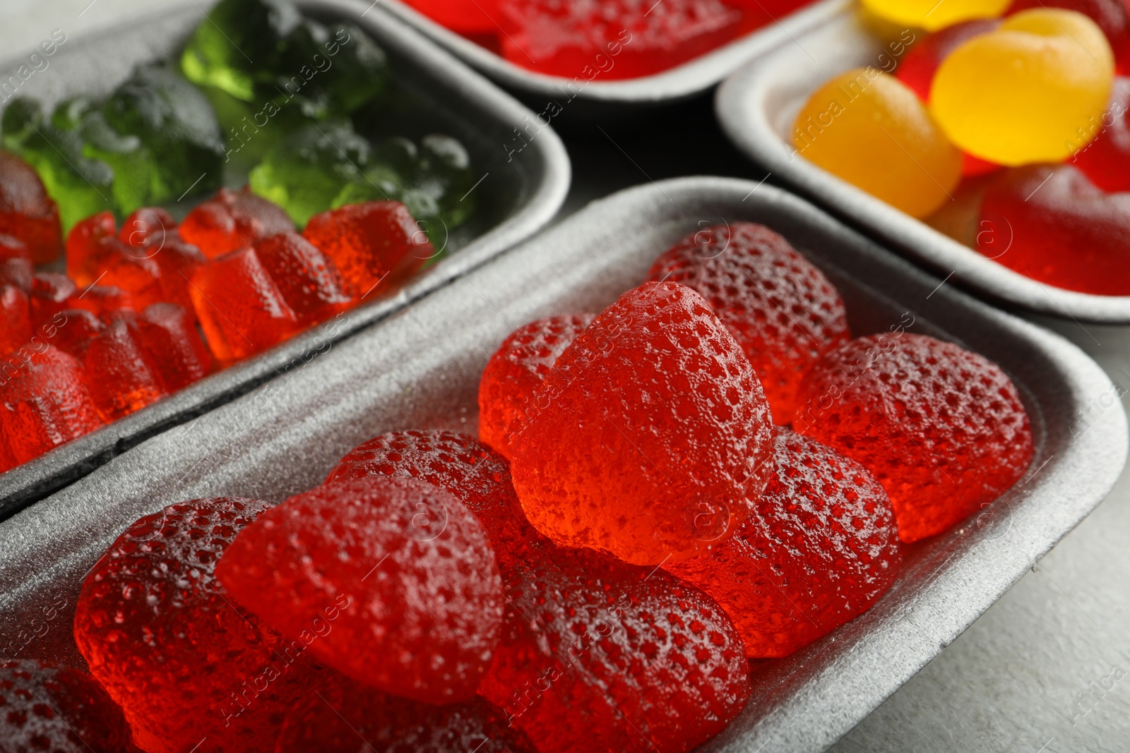 Photo of Different delicious gummy candies on grey table, closeup