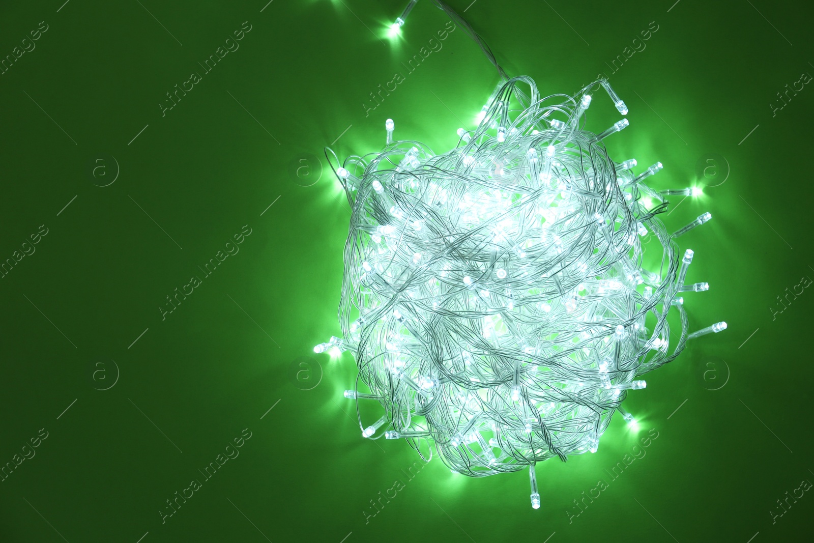 Photo of Glowing Christmas lights on green background, top view Space for text