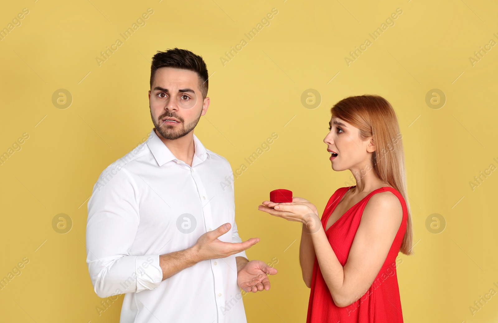 Photo of Young woman with engagement ring making proposal of marriage to her boyfriend on yellow background