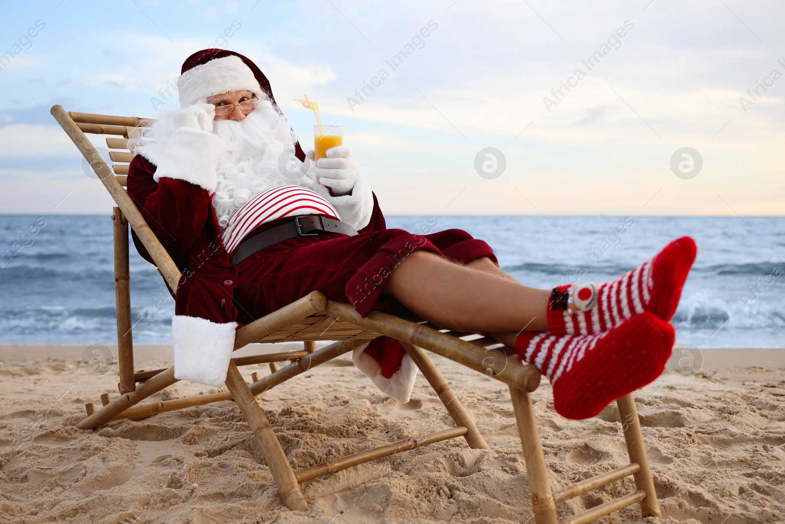 Photo of Santa Claus with cocktail relaxing on beach. Christmas vacation