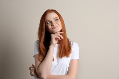 Portrait of thoughtful woman with charming smile and gorgeous red hair on beige background
