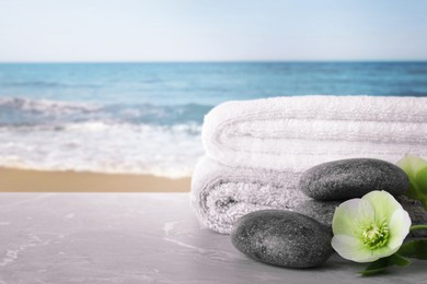 Image of Towels, spa stones and flower on marble table against seascape, space for text