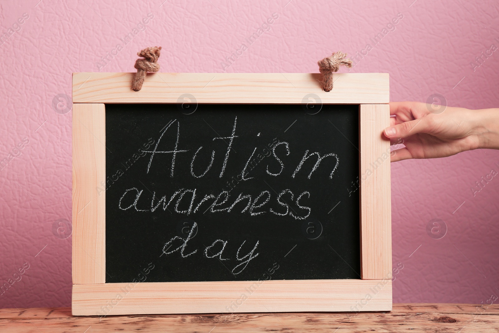 Photo of Woman holding blackboard with phrase "Autism awareness day" on color background