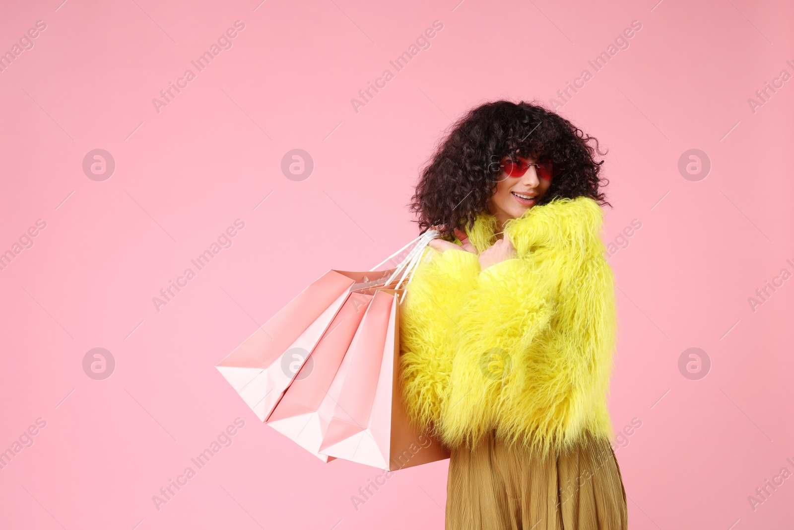 Photo of Happy young woman with shopping bags on pink background. Space for text