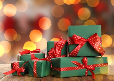 Image of Christmas gift boxes on wooden table against blurred background, bokeh effect