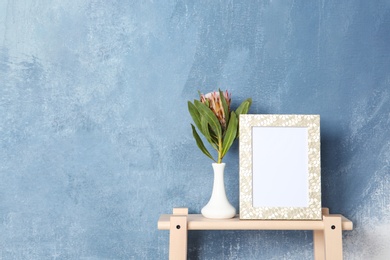 Photo of Blank frame and vase with flower on table near color wall. Mock up for design