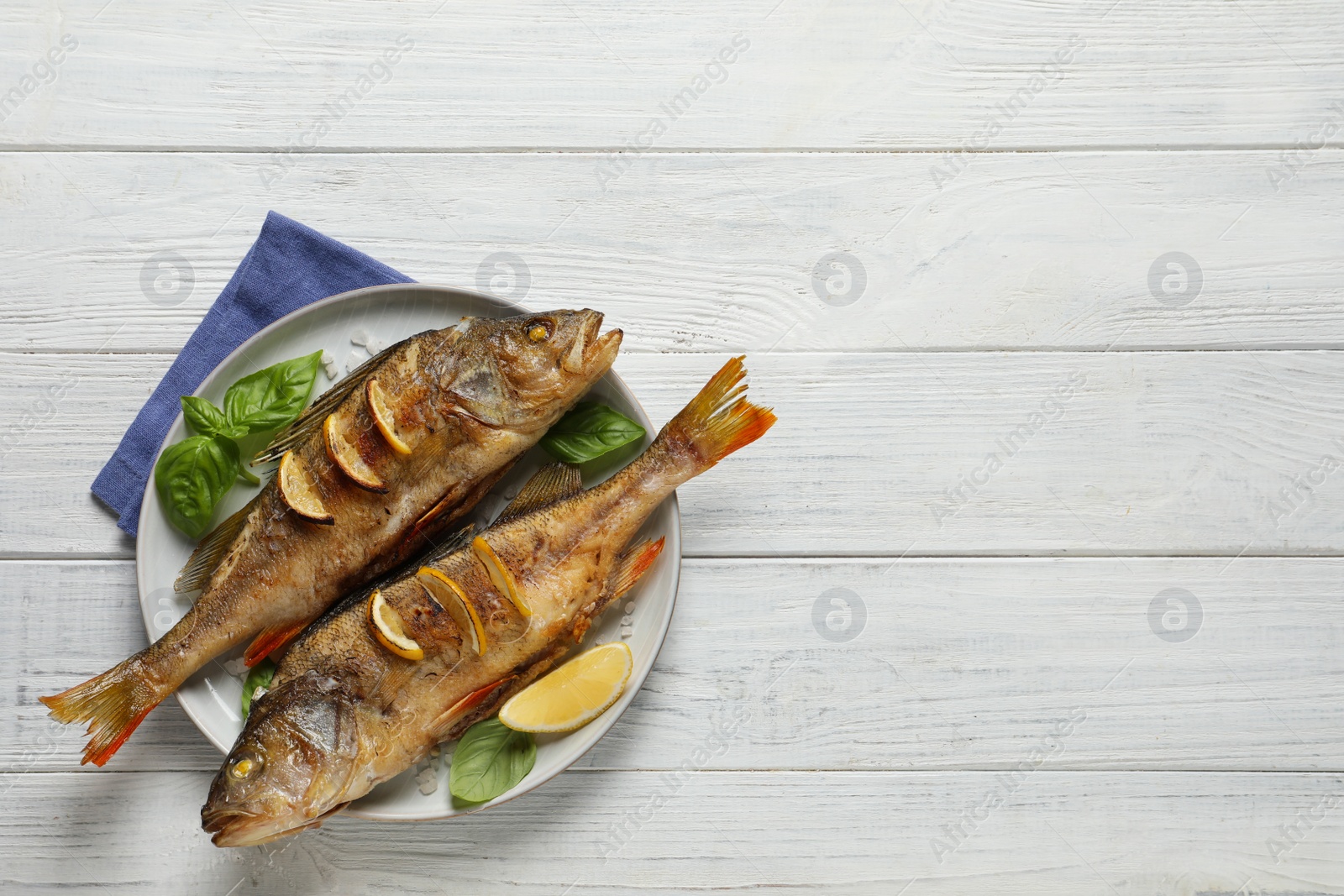 Photo of Tasty homemade roasted perches on white wooden table, top view and space for text. River fish