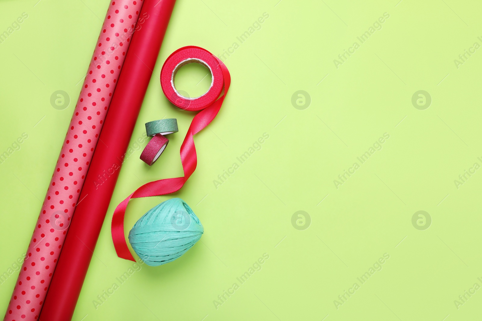 Photo of Rolls of wrapping papers and ribbons on green background, flat lay. Space for text