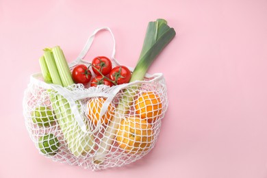 Photo of String bag with different vegetables and fruits on pink background, top view. Space for text