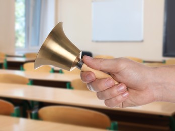 Image of Woman with school bell in empty classroom, closeup