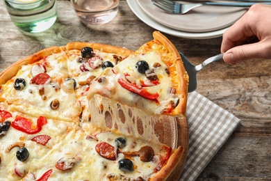 Woman holding shovel with slice of delicious hot pizza over table, closeup