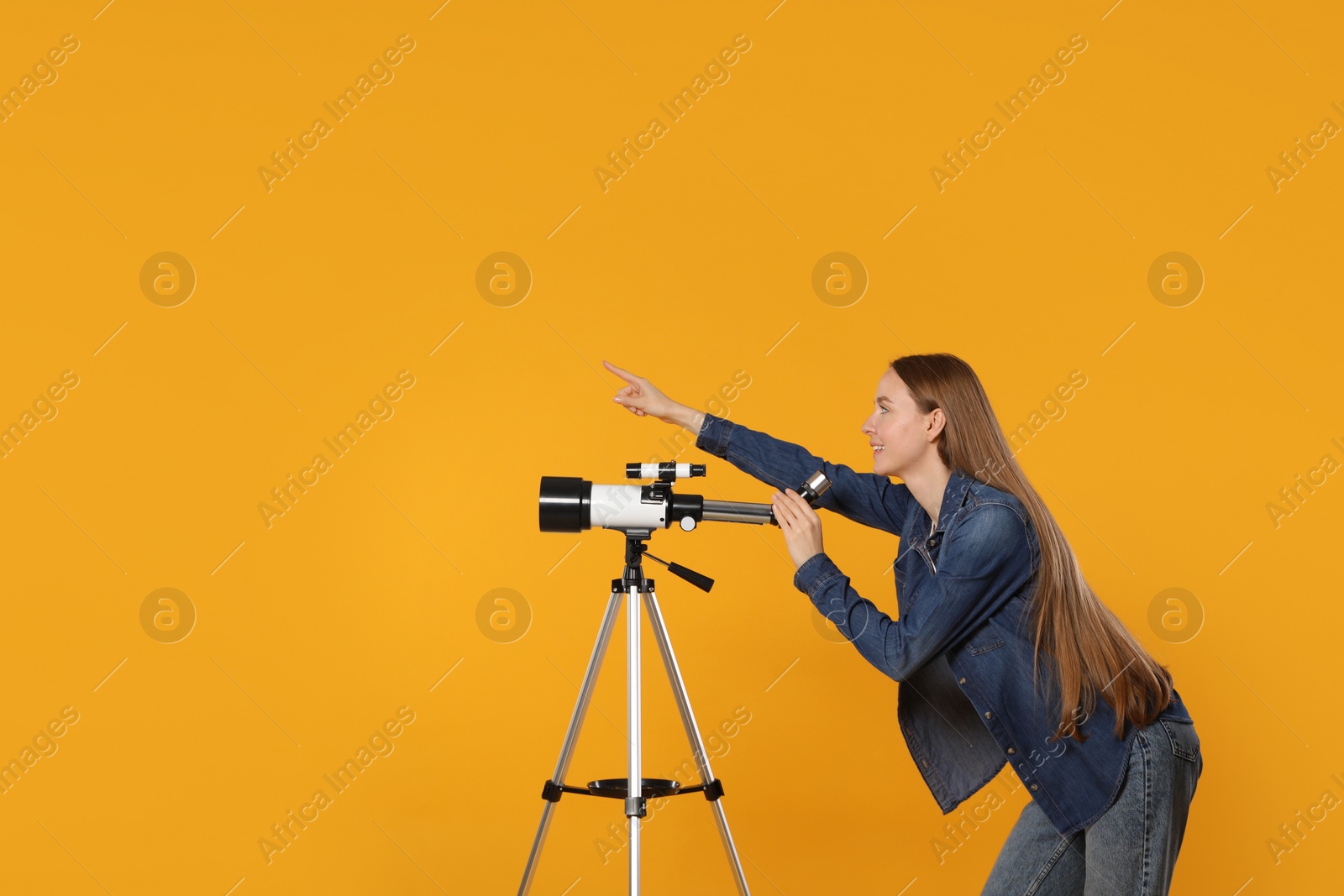 Photo of Young astronomer with telescope pointing at something on orange background, space for text