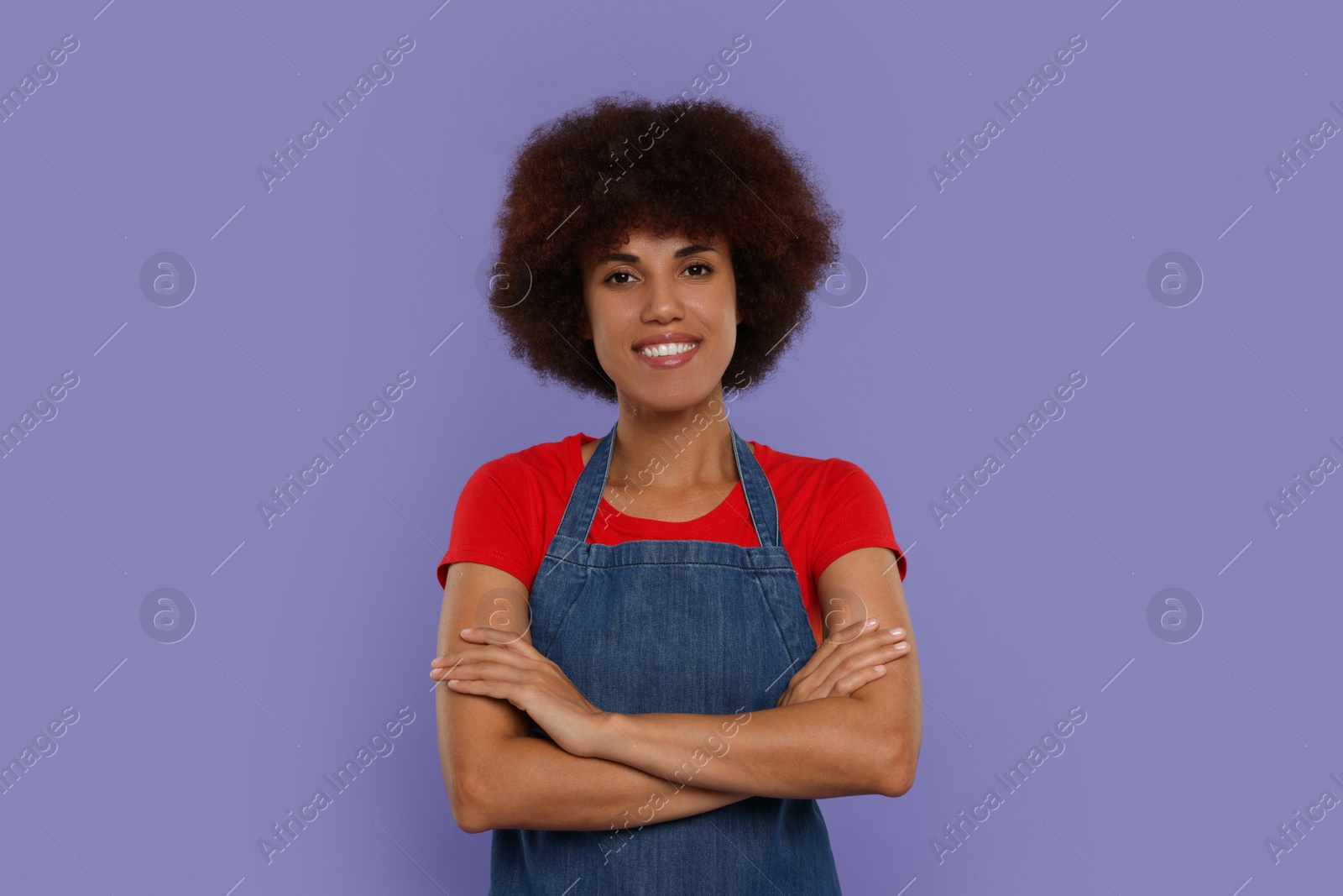 Photo of Portrait of happy young woman in apron on purple background