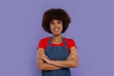 Photo of Portrait of happy young woman in apron on purple background