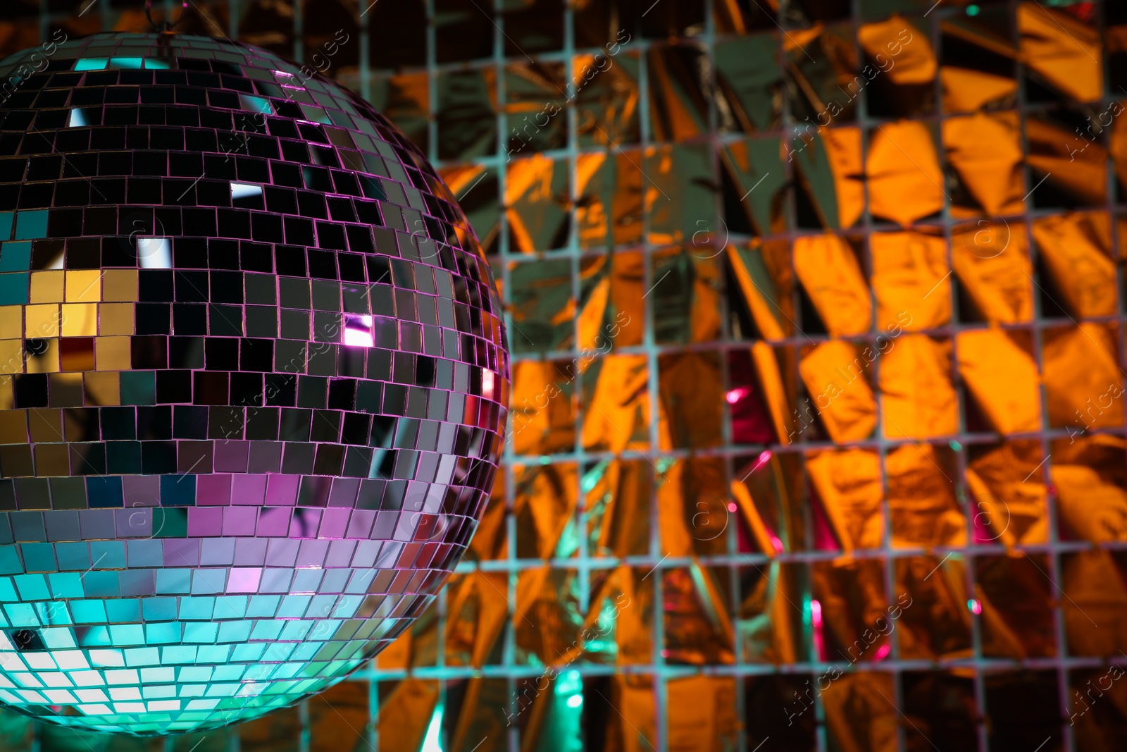 Photo of Shiny disco ball against foil party curtain under turquoise and orange light, space for text