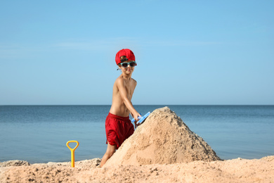 Photo of Cute little child playing with plastic shovel at sandy beach on sunny day