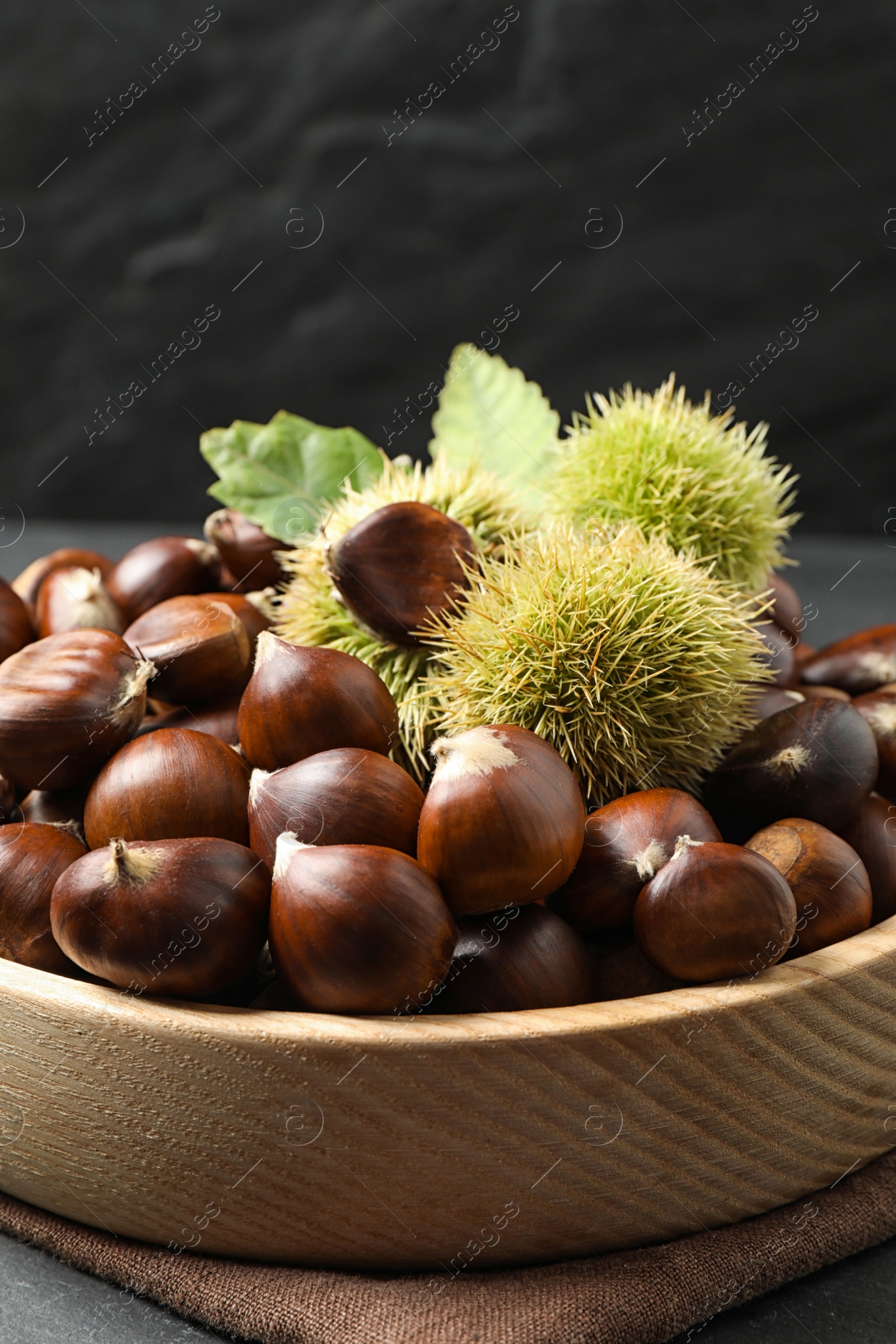 Photo of Fresh sweet edible chestnuts in wooden bowl on table, closeup