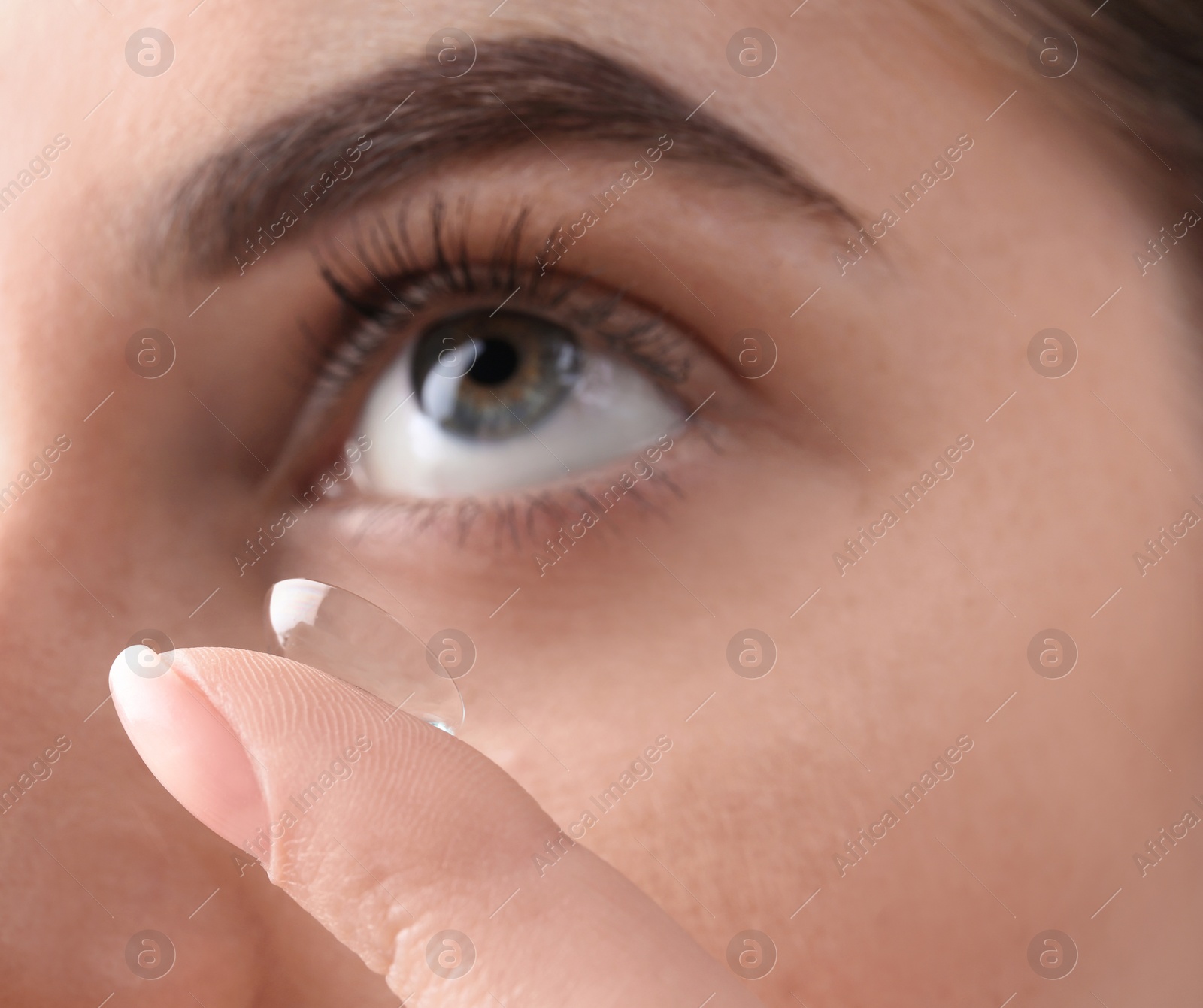 Photo of Young woman putting contact lens in her eye, closeup