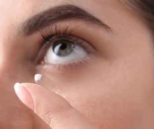 Young woman putting contact lens in her eye, closeup