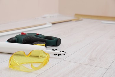 Photo of Plinths, caulking gun, screwdriver, protective glasses and screws on laminated floor in room