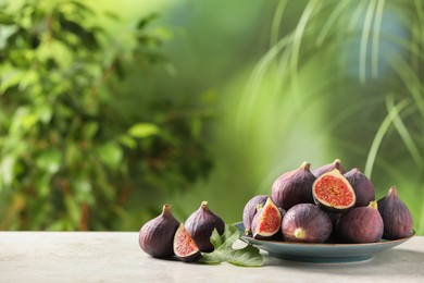 Photo of Plate with fresh ripe figs and green leaf on light table. Space for text