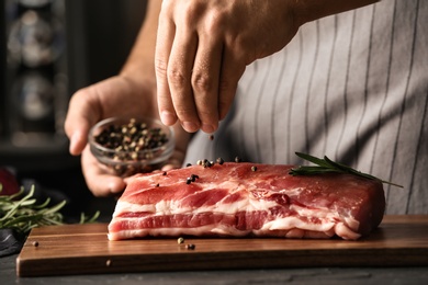 Photo of Man cooking fresh raw meat with pepper and rosemary on table, closeup
